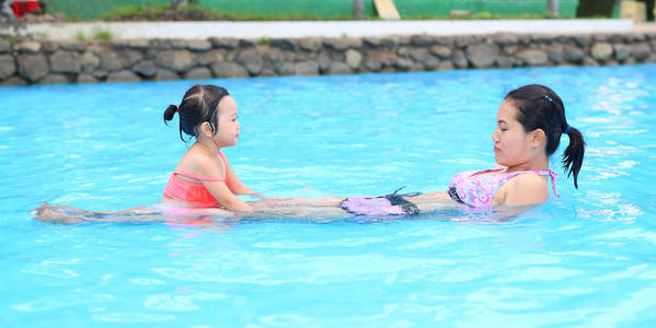 漂亮的小女孩和她的母亲在户外游泳池