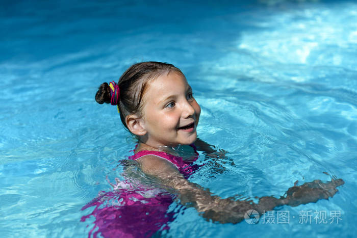 一个小女孩在明亮的绿松石水的游泳池里游泳