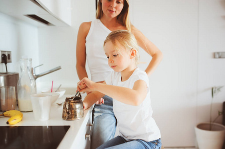 在现代白色的厨房，舒适的生活方式，在早晨吃早饭与孩子女儿在家的母亲