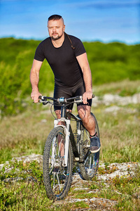 在夏季山上骑山地自行车运动员男人的肖像