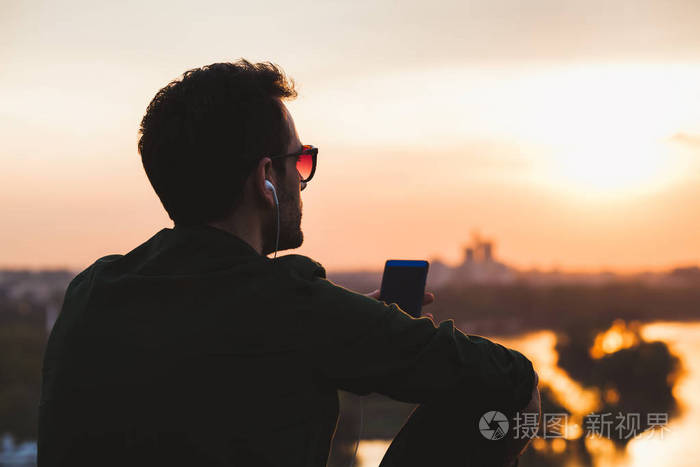 年轻人听音乐在智能手机上的享受夕阳