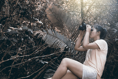 漂亮亚洲女人用双筒望远镜在森林里看