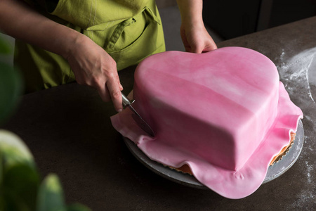 在面包店装饰心形婚礼蛋糕粉红色软糖，无法辨认女人查看从上面
