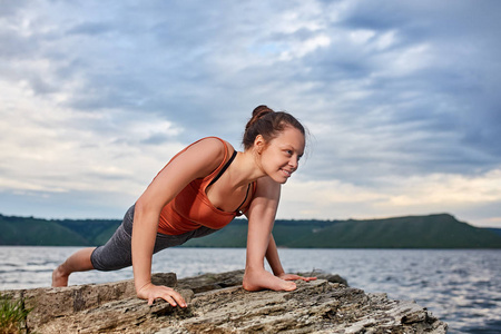 健康的女人对美丽的风景与河岩石上练瑜伽
