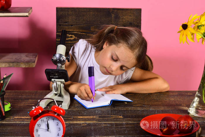 女孩坐在她的办公桌与时钟 显微镜和水果
