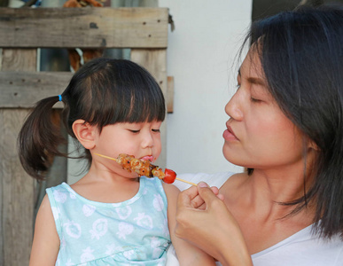 可爱的亚洲宝宝女孩与母亲饮食美味的肉在烧烤时街头食品市场