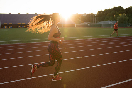 专业运动员在日落时分户外跑步。在体育场户外运动装的女运动员。健身体育活动