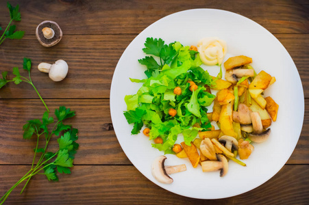 炸土豆烤木桌背景上绿色的莴苣与野生蘑菇在白板上。木制的背景。顶视图。特写