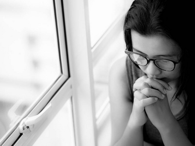 沉默的坐着黑色和白色的伤心女人戴眼镜独自坐着,透过窗户看照片