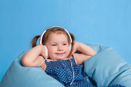 可爱的小女孩，在耳机听音乐使用平板电脑和微笑着坐在蓝色的大袋