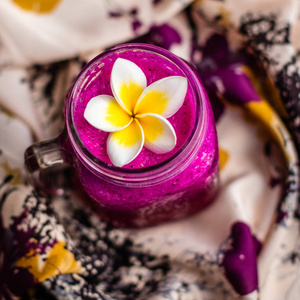 红龙果汁一杯,在用鸡蛋花装饰在华丽的织物.顶视图.方形图像照片