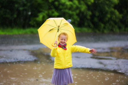 小小的女孩穿着黄色夹克和黄色靴子黄色雨伞在雨中。雨伞的女孩喜欢雨