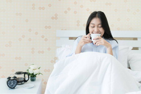 亚洲的年轻女子坐在床上吸烟的同时喝咖啡