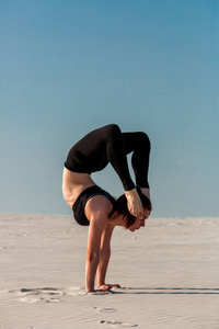 年轻女子练习倒立在海滩与白砂和明亮的蓝天上