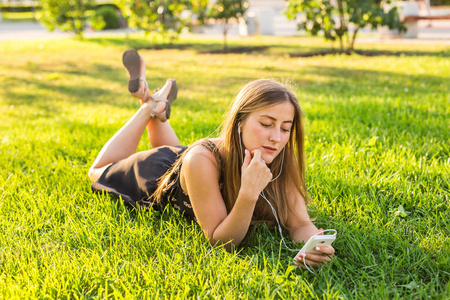 女孩听音乐流戴着耳机在草地上的夏天