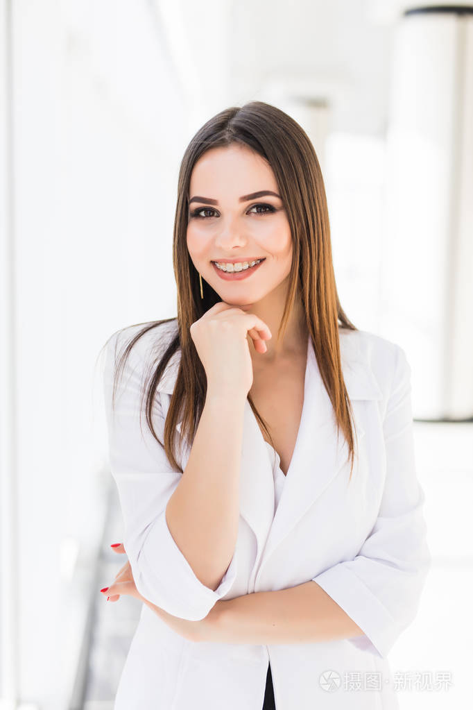 信心十足的年轻商业女人,双臂交叉倚在办公室窗口的肖像