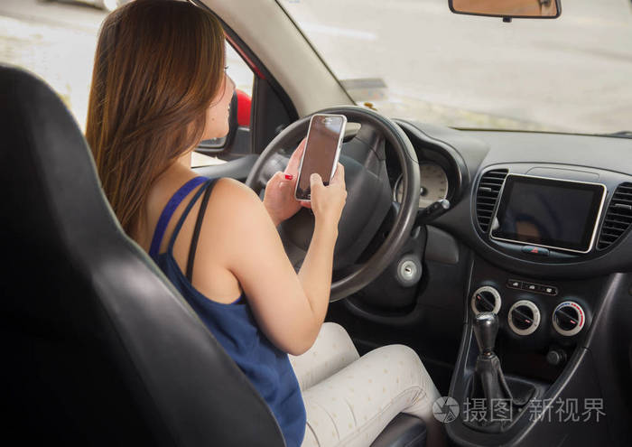 微笑着年轻貌美的女士用她的手机,而自行驾驶的汽车