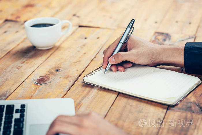 手业务人写作在咖啡厅的木桌上的笔记本
