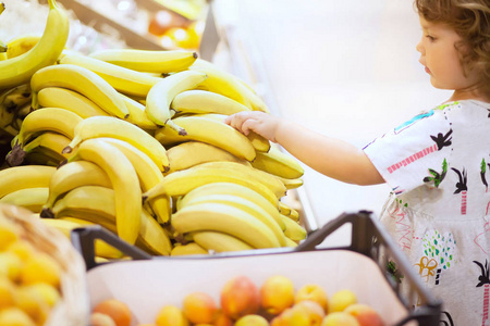 可爱的蹒跚学步女孩在一家食品店选择香蕉果实