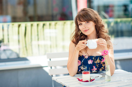 美丽的年轻女子坐在一家咖啡馆。一个女孩喝咖啡和吃甜点。一名年轻女子在城里逛