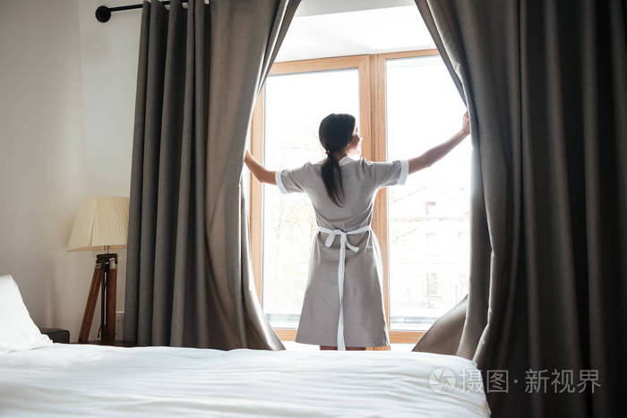 女服务员在酒店的房间里打开窗户窗帘