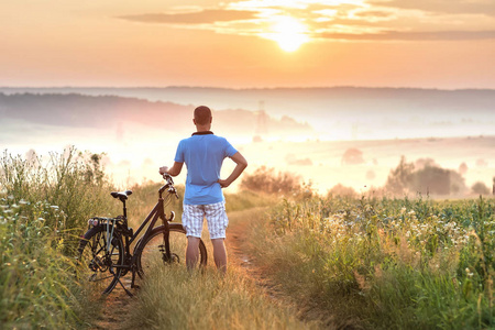 早晨日出与 wonderf 的年轻人站在自行车附近