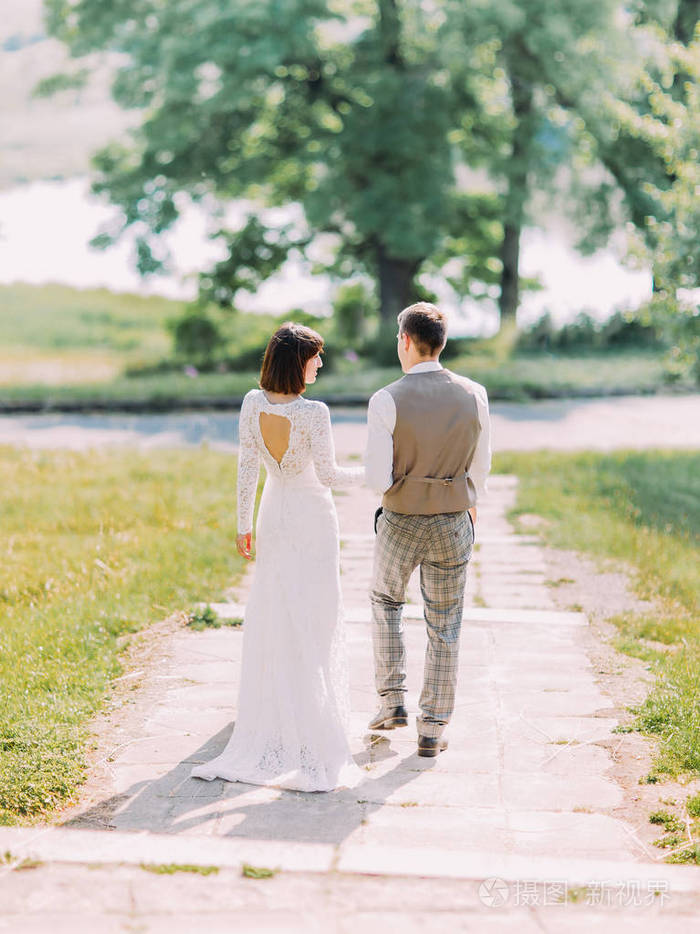 沿着公园步行的新婚夫妇的背影