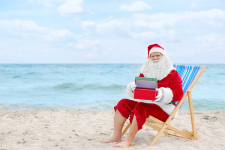 正宗圣诞老人的礼品盒在甲板上的椅子上海滩