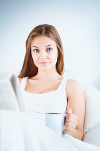 年轻漂亮的女人在床上看报，享受一杯茶