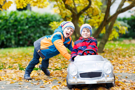 两个快乐的双胞胎孩子玩乐和大老玩具车在秋天的花园里玩的男孩
