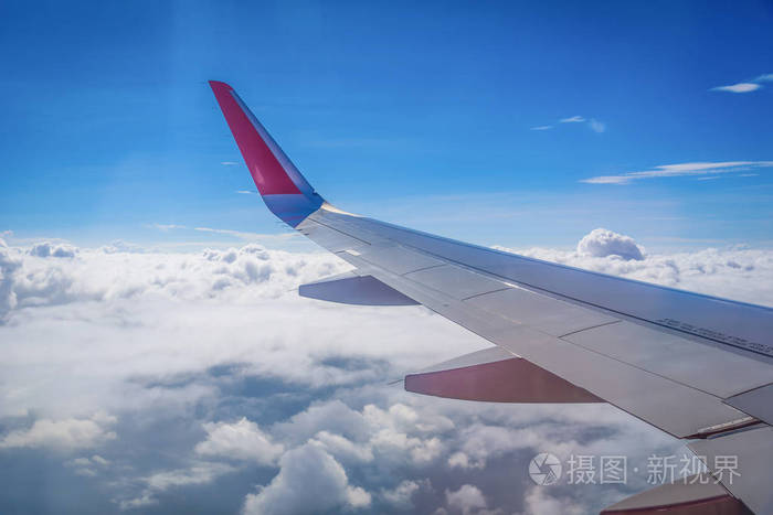在蓝色天空背景下通过窗口在云层上面飞行的飞机的翅膀