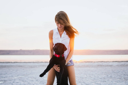 年轻女性在日落时分与拉布拉多狗在沙滩上拥抱