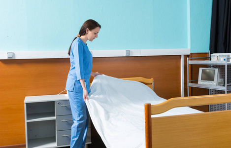 女护士在蓝色均匀改变医院的床上的床单