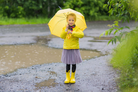 甜美的女孩下一把伞在大雨，站在一个水坑里