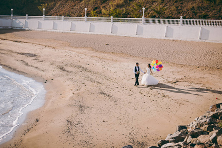 新婚夫妇与球沿着海边散步