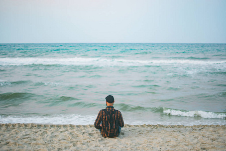 在黎明时的海洋背景下坐在一个年轻白色旅游人。旅游和生活方式的概念