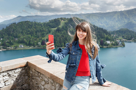 女孩从山谷景观与背景上的湖山城堡顶部采取自拍照。看着相机