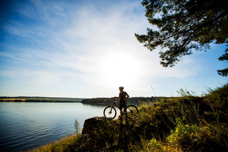 侧面的骑手骑着自行车站在一块岩石上，欣赏落日美景。动机和创造灵感的冒险