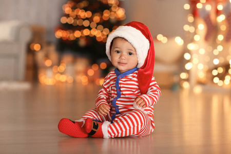 可爱的小宝宝与圣诞老人的帽子在地板上和背景上的模糊的圣诞灯。