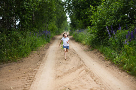 乡村小路沿这条乡村小路的农村景观在赤脚跑步的可爱微笑小女孩照片