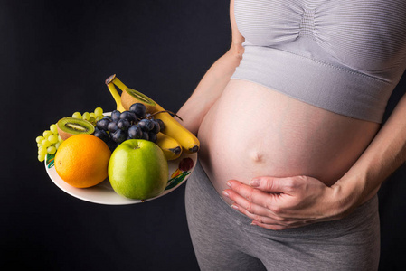 孕妇腹部拿着盘子里的水果。为控制体重和怀孕期间的健康饮食概念