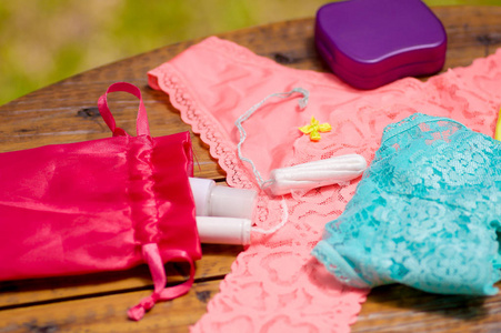 封闭的月经棉卫生棉条粉色和蓝色的女人内衣和红色棉布袋，在木桌前和一个紫色的塑料盒，在模糊的背景