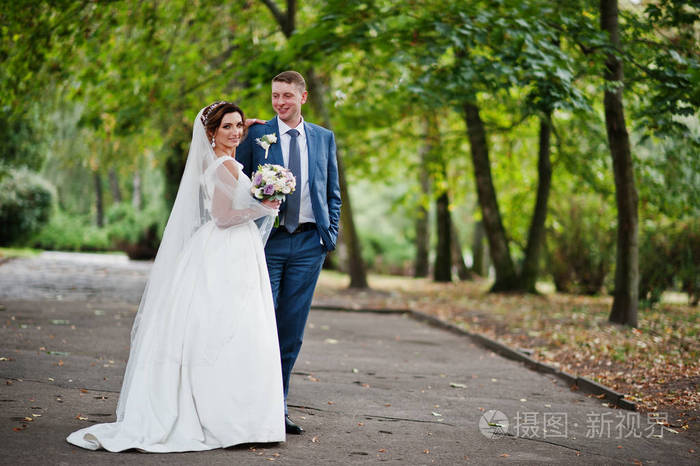 神话般的年轻新婚夫妇摆在阳光明媚的大街上的公园