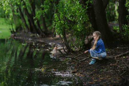 在她的手，小女孩正坐在池塘边用一根棍子。假期。娱乐