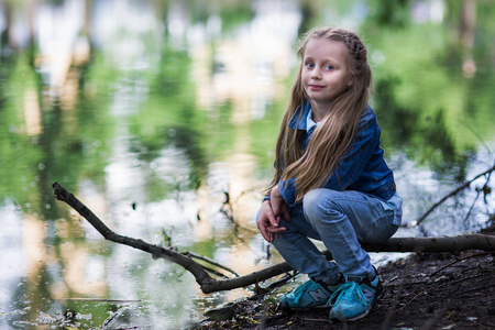 小女孩正坐在池塘边。假期。娱乐