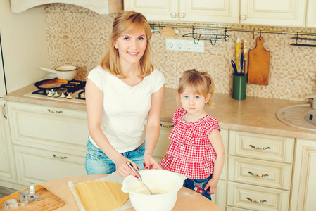 年轻的母亲和可爱的小女儿准备面团烘制饼干和乐趣在厨房里
