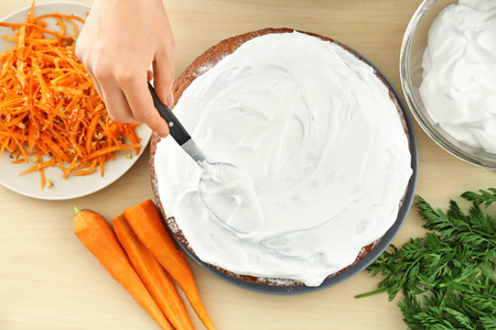 女人在厨房里的胡萝卜蛋糕上涂抹奶油