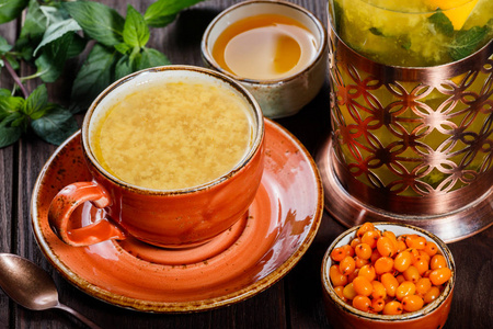 与海杯连碟，沙棘茶配复古茶壶 新鲜浆果 蜂蜜 薄荷上深色木制背景。健康饮料