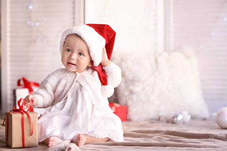 可爱的小宝宝与圣诞老人的帽子及礼品盒坐在地上模糊背景