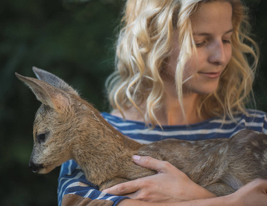 年轻漂亮的女人,在森林中拥抱动物獐鹿小鹿照片
